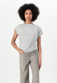 Top grigio a maniche corte con vestibilità rilassata e dettaglio con cordino alla spalla. Abbinato a pantaloni beige a vita alta.