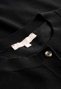 Schwarze Strickjacke aus weichem Strickstoff, mit Rundhalsausschnitt, gerippten Bündchen und einem runden Knopfdetail mit einem subtilen Glanz.