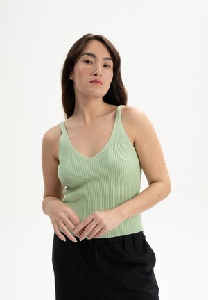 Lichtgroen ribbel tanktop met een v-hals, slanke spaghettibandjes en een aansluitend silhouet. Draagt met zwarte broek, die een gestructureerde brei toont.