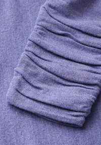 Top in tessuto viola con maniche arricciate, caratterizzato da una texture morbida e una finitura melange discreta. Il design evidenzia il ruching lungo il braccio.
