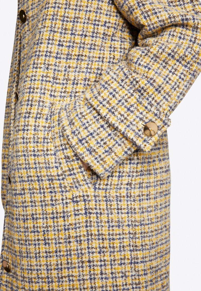 Abrigo de mezcla de lana en patrón de cuadros amarillo, azul y blanco. Presenta una superficie texturizada y acentos de botones en tono dorado en los puños y en la parte frontal.