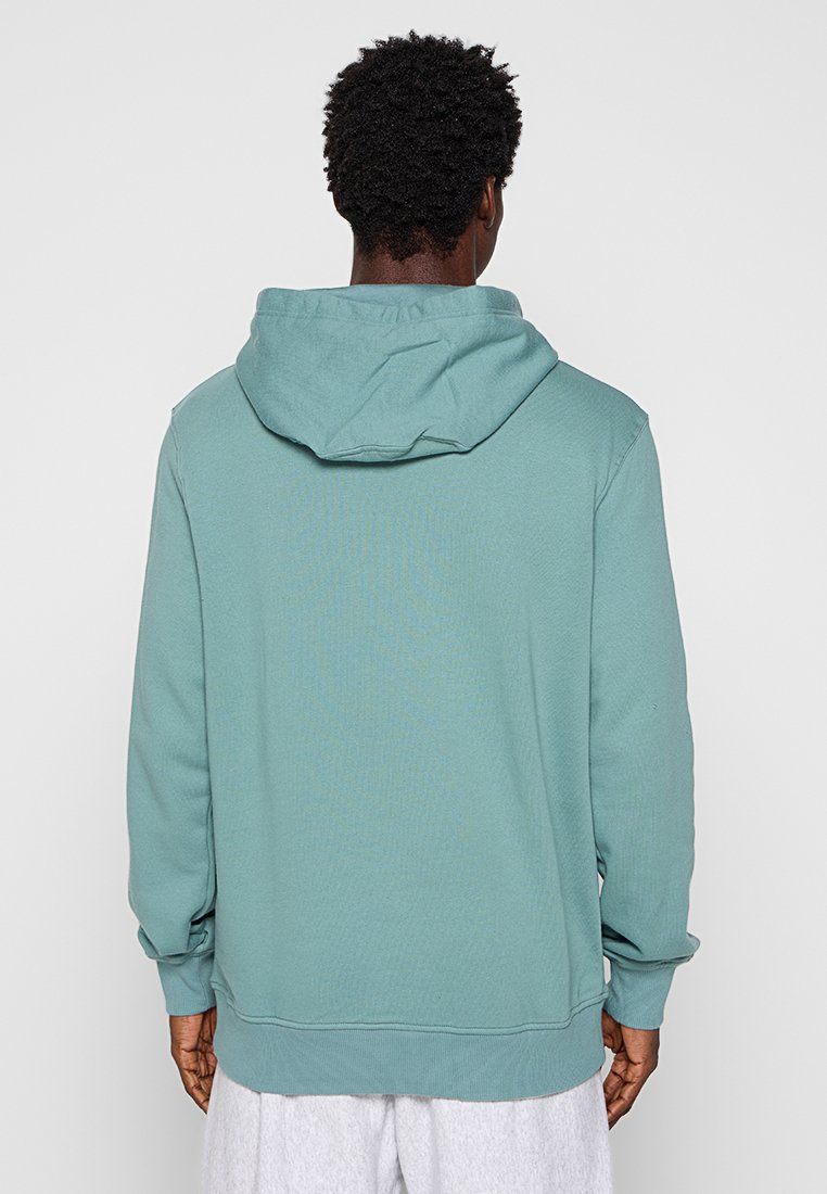Sweatshirt à capuche en teal, fabriqué en tissu doux. Il possède une poche kangourou et des poignets côtelés, avec une coupe décontractée.