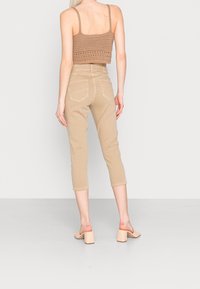Béžové zkrácené kalhoty vyrobené z bavlny, se slim fit střihem, mají zadní kapsy a ohrnuté lemy. Jsou nošeny s hnědým pleteným crop topem a podpatky.