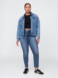Casaco de denim em azul claro com um corte ligeiramente oversized, apresentando dois bolsos no peito e um colarinho clássico, combinado com jeans skinny azul escuro.