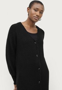 Zwarte gebreide cardigan met een diepe V-hals, lange mouwen en vijf zwarte knopen aan de voorkant. Gelaagde, zachte stof.