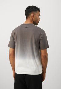 Kortærmet t-shirt i gradient fra grå til hvid, med en blød tekstur og et diskret adidas-logo på ryggen ved nakkekanten.
