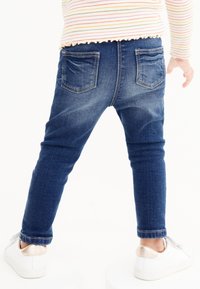 Jean en denim bleu à coupe slim, avec des poches arrière et un léger effet délavé. Associé à des baskets blanches et un t-shirt à manches longues rayé.
