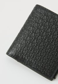 Black wallet made of textured leather, featuring an embossed pattern of interlocking letters, with a smooth edge and zipper detail.