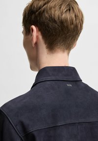 Navy suede jacket featuring a subtle collar, clean lines, and a small logo on the back, conveying a smooth texture and modern design.