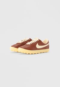 Brązowe skórzane trampki z kremowymi akcentami, z zaokrąglonym noskiem, kontrastową żółtą podeszwą i tradycyjnym sznurowaniem.