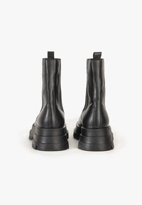 Svarta läderankel stövlar med en kraftig sula, texturerad yta och dragflikar baktill, med sömnadsdetaljer längs sidorna.