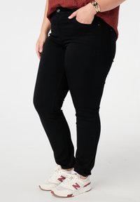 Zwarte skinny jeans van denim, met een hoge taille, zakken en een voorknopsluiting, gecombineerd met witte en bordeauxrode sneakers.