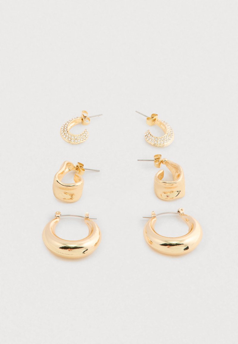 Tres pares de pendientes de aro de oro en estilos pequeño con perno, mediano grueso y grande liso dispuestos sobre un fondo claro y simple.