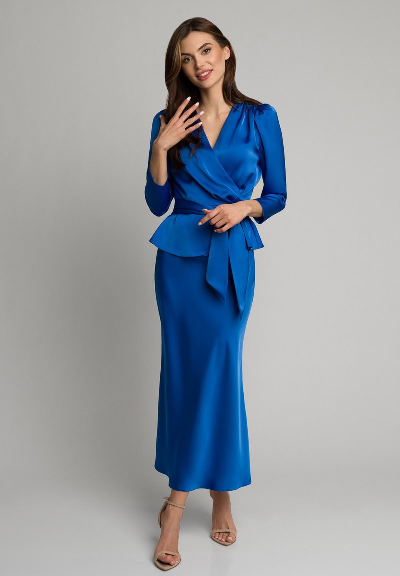 Niebieska satynowa sukienka o kroju kopertowym z peplum w pasie, długimi rękawami i paskiem do wiązania. Elegancka sylwetka o gładkiej fakturze.