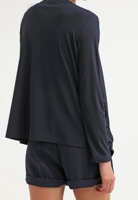 Mörkblå avslappnad topp med långa ärmar och sidsprund, matchad med shorts med rullad fåll. Slätt, lättviktigt tyg.