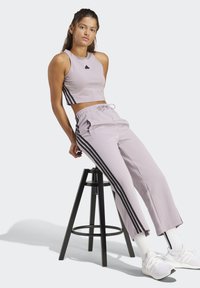 Hellblaues, gekürztes Tanktop mit schwarzem Dreieckslogo und schwarzen Seitenstreifen, kombiniert mit passenden lila Jogginghosen mit schwarzen Streifen.