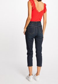 Jean bleu marine taille haute à coupe effilée, comprenant cinq poches et une couture contrastée, associé à un haut rouge orné de dentelle.