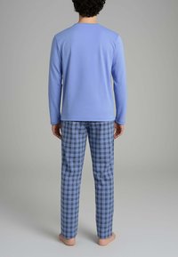 Maglietta azzurra a maniche lunghe con colletto rotondo, abbinata a pantaloni a quadri blu con righe nere. Tessuto morbido, vestibilità comoda, senza loghi visibili.