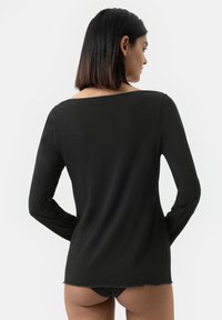 Chemise noire à manches longues en tissu lisse avec un décolleté large et des détails discrets en bas, mettant en valeur une silhouette ajustée vue de dos.