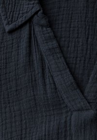 Dunkel marineblaues, strukturiertes Gewebe mit einer zerknitterten Oberfläche, das einen Kragen und ein V-Ausschnitt-Design aufweist. Der Stoff zeigt ein Rippmuster.