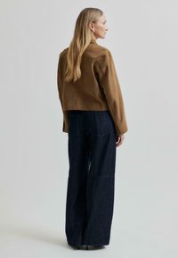 Barna velúr cropped dzseki hosszú ujjakkal, sötét farmer széles szárú nadrággal párosítva. Simább textúra, minimalista részletezés, egyszerű dizájn.