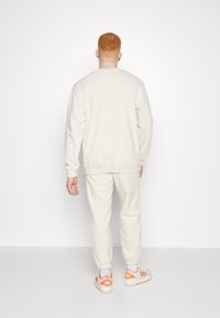 Sudadera de color crema en tamaño grande y pantalones de chándal en una tela suave. La sudadera tiene puños acanalados; los pantalones presentan tobillos con elástico y bolsillos laterales.