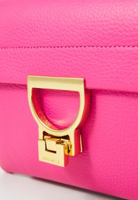Pink leather handbag featuring a gold metallic clasp with a circular handle. Textured surface with subtle stitching details.