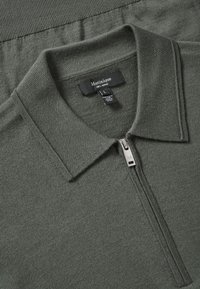 Merino volna polo majica v temno zeleni barvi z kratkim zadrgo in rebrastim ovratnikom. Ima teksturiran, pleten vzorec in oznako z velikostjo L.