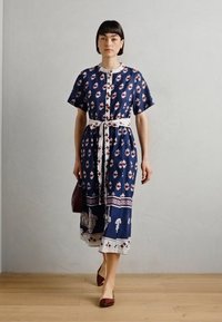 Blå mønstrete kjole med korte ermer, detaljert kant og hvitt belte. Stoffet har blomster- og geometriske design. Brukt med maroon ballerinas.