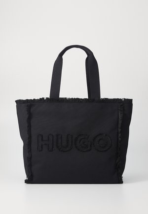 Czarna torba typu tote z materiałowymi uchwytami, na której znajduje się napis "HUGO" w podniesionych, teksturowanych literach oraz postrzępione brzegi przy szwach.