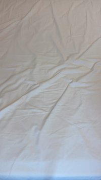 Țesătură de bumbac alb, cu o textură netedă, prezentând cute și pliuri, specifică unei cearșaf. Fără modele sau detalii suplimentare.