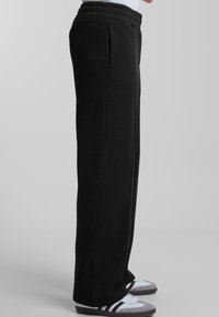 Black sweatpants made of soft fabric, featuring a relaxed fit, side pockets, and cuffs at the hem. Simple and functional design.