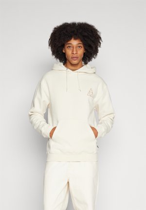 Sudadera beige fabricada en un material suave, con un bolsillo frontal, capucha con cordón y un pequeño logotipo geométrico en el lado izquierdo del pecho.