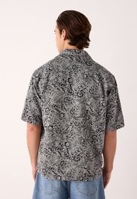 Camicia a maniche corte con stampa paisley in bianco e nero, caratterizzata da un colletto rilassato e un orlo dritto. Realizzata in tessuto leggero.