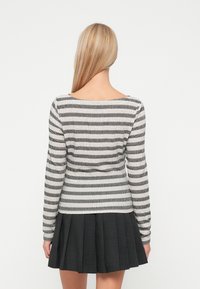 Sweter w paski, dziany, z długim rękawem w odcieniach szaro-białych, zestawiony z plisowaną czarną spódnicą. Miękka tekstura, dopasowany krój, okrągły dekolt.