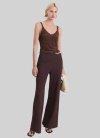 Débardeur scintillant marron avec un décolleté en V et des bretelles fines, associé à un pantalon large taille haute de couleur marron foncé. Le modèle tient un sac en osier.