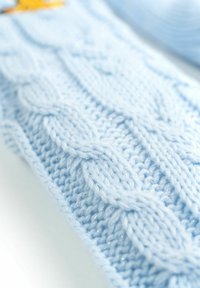 Tessuto a maglia azzurro chiaro con un motivo a cavo testurizzato e un sottile luccichio. Il focus ravvicinato rivela una texture morbida e pelosa con punti intricati.