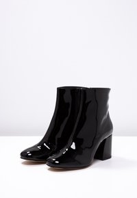 Black patent leather ankle boots with block heels and side zippers, displayed on a white surface against a plain background.