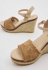 Sandalias de cuña con un upper tejido en tono marrón que presenta intrincados bordados, una correa para el tobillo beige y un tacón envuelto en yute texturizado.