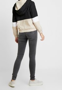 Kurtka w kolorowym blokowym wzorze w czerni, beżu i bieli, z elastycznym obszyciem na dole i mankietach. Noszona z szarymi obcisłymi dżinsami i jasno kolorowymi trampkami.