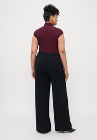 Top burdeos de manga corta con cuello alto, combinado con pantalones amplios negros. Textura suave con caída delicada. Zapatos negros de tacón.