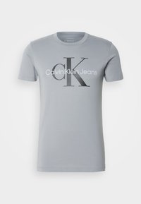 Light gray cotton t-shirt with short sleeves, featuring a black graphic print of "Calvin Klein Jeans" and a large "CK" logo.
