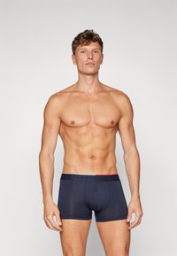 Caleçons boxers en tissu bleu marine foncé avec un ajustement près du corps. Dotés d'une ceinture en noir contrasté avec des accents rouges et blancs. Texture lisse.