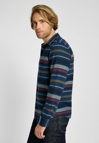 Camicia a maniche lunghe di colore blu navy con righe orizzontali grigie, verdi e rosse. Colletto e taschino sul petto; realizzata in tessuto morbido.
