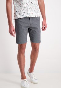 Pantaloni shorts grigi realizzati in un tessuto morbido, con un design semplice a taglio dritto e una singola tasca anteriore. Indossati con una camicia a fantasia.