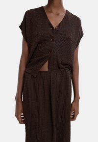 Brązowy, teksturowany dwuczęściowy zestaw składający się z krótkiego rękawa topu z dekoltem w kształcie litery V i zapięciem na guziki, w zestawie z pasującą spódnicą do kostek.