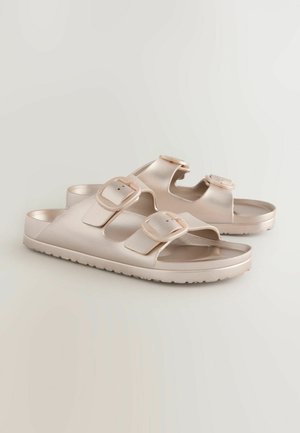 Lys beige sandaler med to justerbare spænder. Lavet af glat, skinnede materiale med en flad sål og tekstureret yders�ål for godt greb.