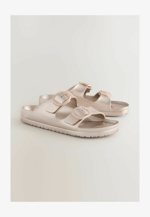 Lys beige sandaler med to justerbare spænder. Lavet af glat, skinnede materiale med en flad sål og tekstureret ydersål for godt greb.