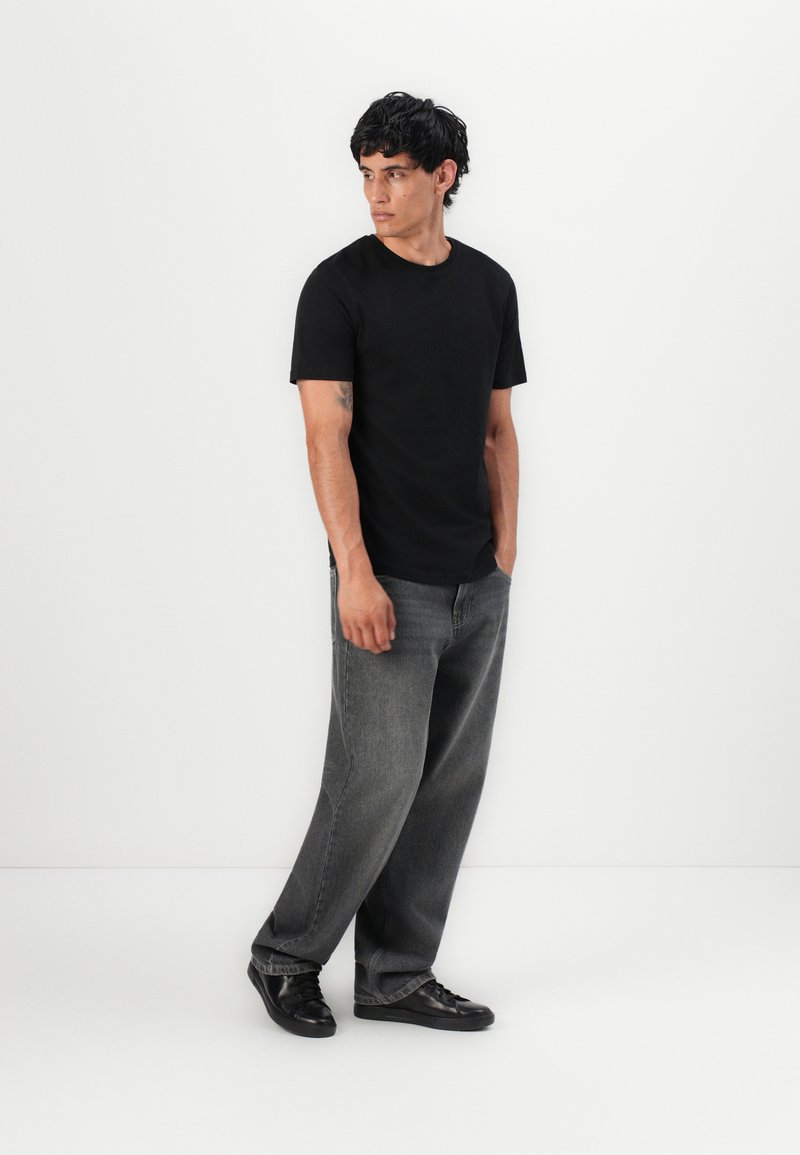 Black t-shirt with short sleeves, paired with loose-fit gray jeans and black sneakers. Plain design, minimal detailing, smooth texture.