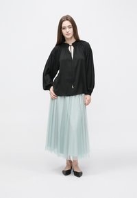 Čierna blúzka s výstrihom do tvaru kvapky a nariasenými ramenami, skombinovaná so svetlomodrou tylovou sukňou. Oblečenie je doplnené čiernymi balerínami.